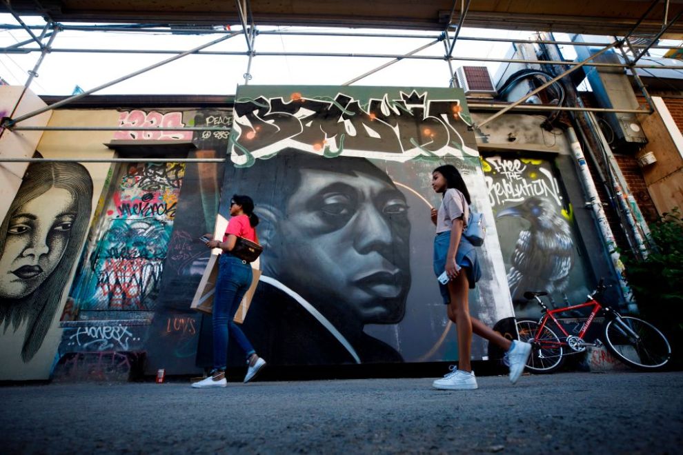 People walk by a mural of late US novelist and activist James Baldwin (C) in Graffiti Alley in Toronto, Ontario, Canada, June 11, 2020. - The well known Toronto alleyway is being painted with prominent Black figures and messages of solidarity against anti-black racism in support of the Black Lives Matter movement. (Photo by Cole BURSTON / AFP) / RESTRICTED TO EDITORIAL USE - TO ILLUSTRATE THE EVENT AS SPECIFIED IN THE CAPTION